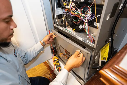 Technician servicing furnace with multimeter and wires for safe HVAC operation at Acosta Heating, Cooling & Electrical.