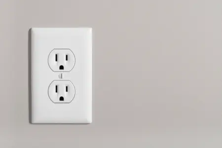 White electrical outlet installed on a light gray wall, illustrating safe electrical installation relevant to surge protection and outdoor electrical solutions.