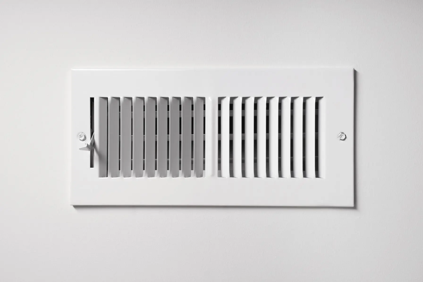 Air vent cover on a white wall, illustrating HVAC air circulation system related to heat pump maintenance and indoor climate control.