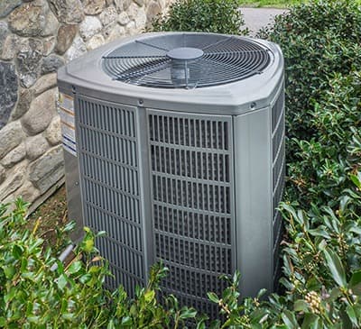 Air conditioning unit with grid exterior among stone wall and greenery by Acosta Heating, Cooling & Electrical.