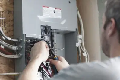 Electrician working on wiring inside a residential electrical panel.