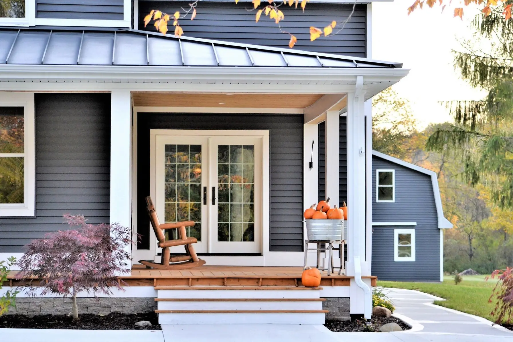 Modern country home entrance with a rocking chair and decorative pumpkins on the porch, showcasing a welcoming atmosphere for winter home maintenance and comfort.