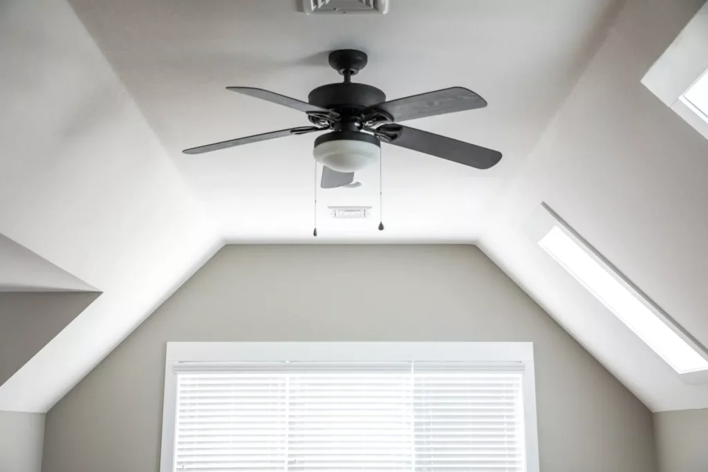 Ceiling fan installed in a modern room with sloped ceiling, showcasing stylish design and natural light from skylights, enhancing home comfort and energy efficiency.