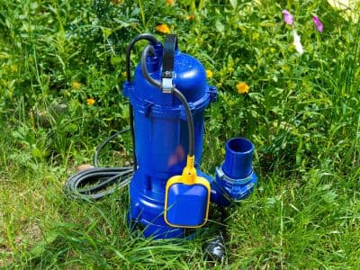 Blue sump pump on grass, featuring a float switch, essential for preventing basement flooding and water damage during heavy rainfall and snow thaws.