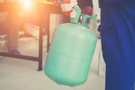 Professional HVAC technician handling a refrigerant tank during a residential air conditioner repair and maintenance call.