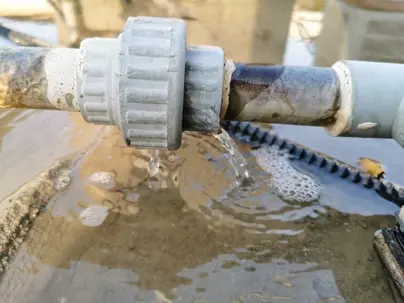 A leaking plumbing joint on a PVC pipe showing water escaping from the coupling connection, indicating a faulty seal or crack.