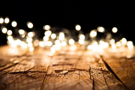 Abstract background texture featuring a sharp focus on cracked wood grain fading into bright, out-of-focus golden fairy lights.