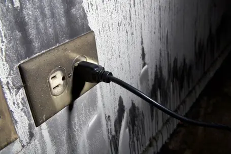 Burned and charred wall outlet with a black cord plugged into it, showing signs of severe electrical fire damage.