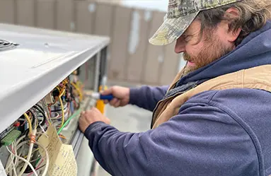 Technician performing HVAC maintenance, working on air conditioning unit wiring, showcasing expertise in heating and cooling services.