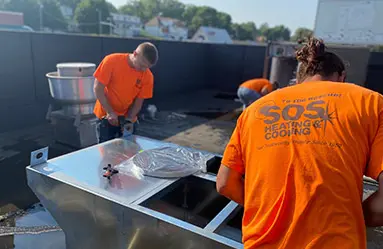 Technicians from SOS Heating & Cooling working on HVAC installation on a rooftop, wearing orange shirts with the company logo, showcasing professional service in Omaha.