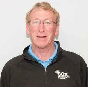 Greg from SOS Heating & Cooling, wearing a black jacket with the company logo, smiling against a plain white background.