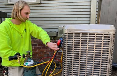 Technician servicing an outdoor air conditioning unit, wearing a bright green shirt, demonstrating HVAC maintenance services for SOS Heating & Cooling in Omaha, NE.