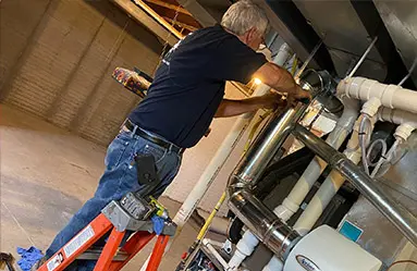 Technician performing HVAC maintenance on ductwork while using a ladder in a basement setting, highlighting professional heating and cooling services by SOS Heating & Cooling.
