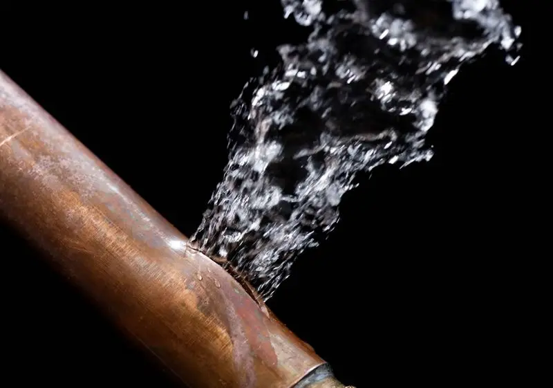 Bursting copper pipe with water spraying, illustrating emergency plumbing repair needs in winter preparation for homeowners in New Jersey.