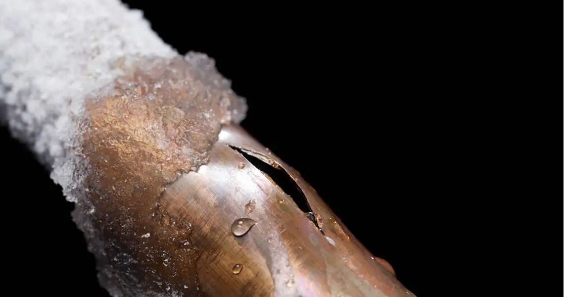 Frozen copper pipe with cracks and ice on a dark background, highlighting plumbing damage by Jeffrey Burke Plumbing Services.