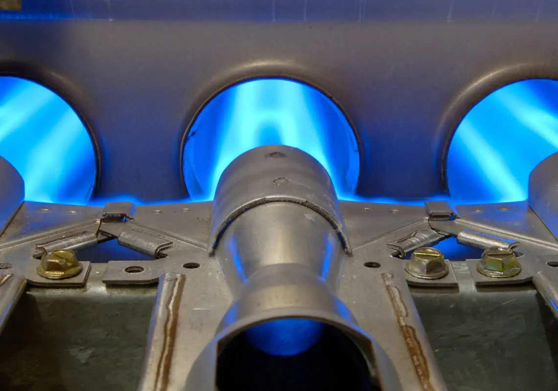 Close-up of a furnace burner with blue flames, illustrating heating system functionality for winter preparation by Jeffrey Burke Plumbing, Heating & Cooling.
