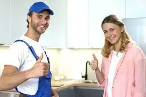 Plumber and satisfied customer giving thumbs up in a modern kitchen, highlighting plumbing services and touchless faucet technology.