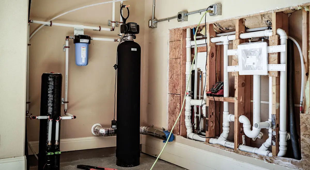 Water filtration system installation featuring a blue filter, black tank, and white PVC piping, showcasing plumbing solutions by American Eagle Plumbing.