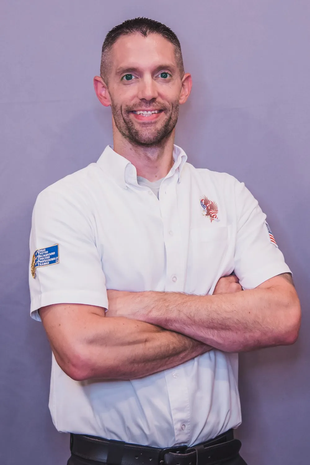 American Eagle Plumbing team member in a white shirt with logo, smiling and posing with arms crossed against a neutral background.
