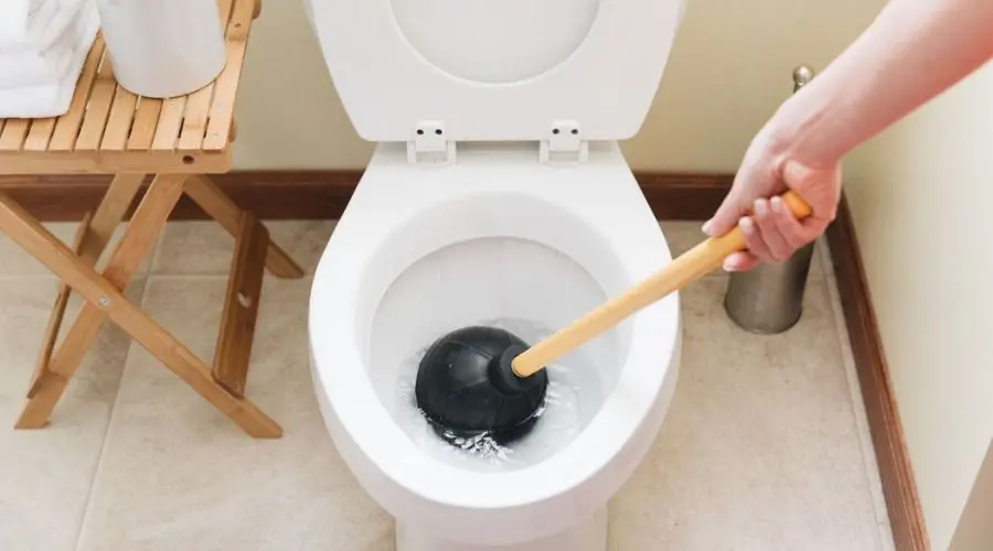 Person using a plunger to unclog a backed-up toilet, emphasizing plumbing repair and maintenance in a home setting.