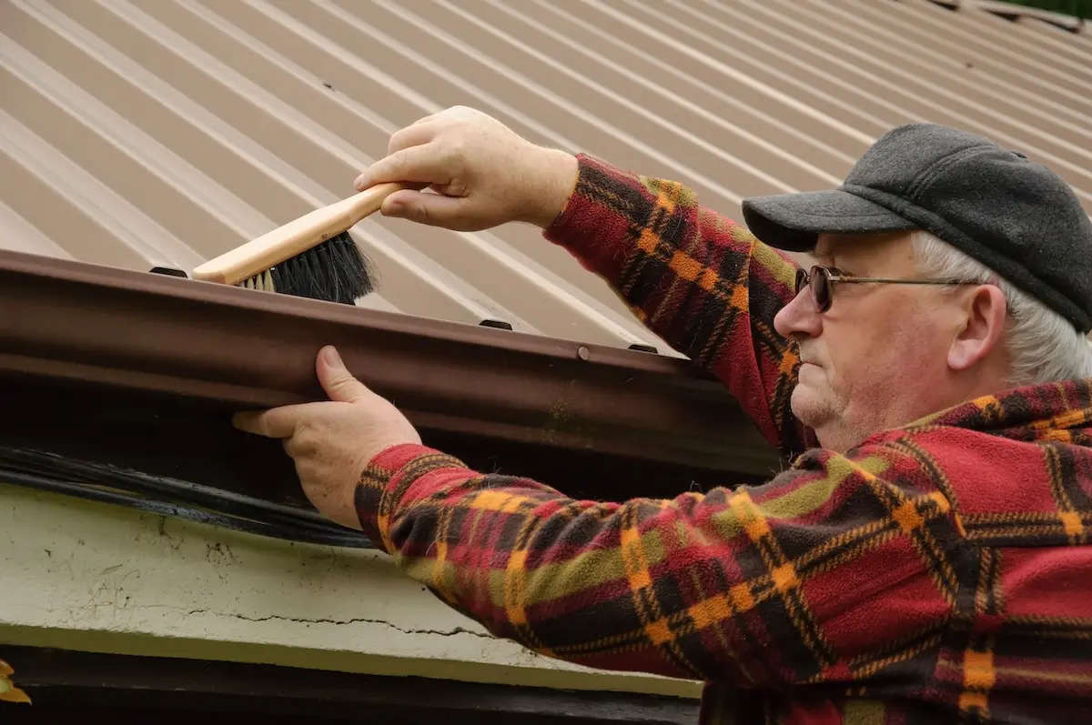 senior male cleaning out the shed gutter with brush
