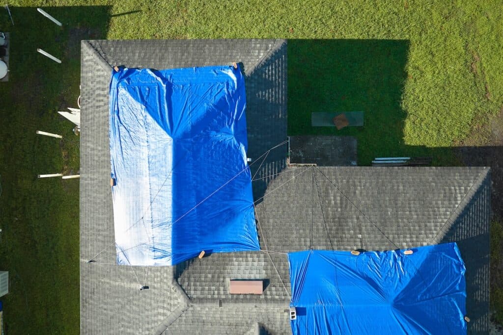 Top view of leaking house roof covered with protective tarp sheets 