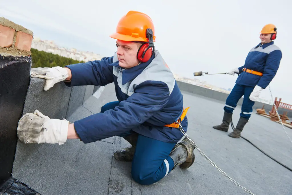 Roofers installing flat roof materials using membrane system and safety gear on commercial roof