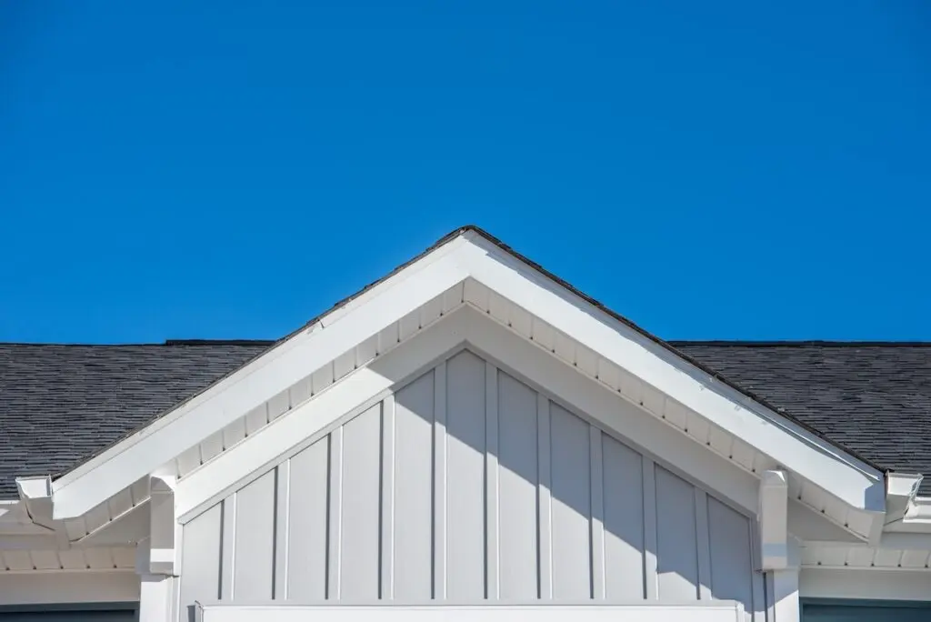 Gable roof with white fascia, gray vertical vinyl lap siding blue sky background