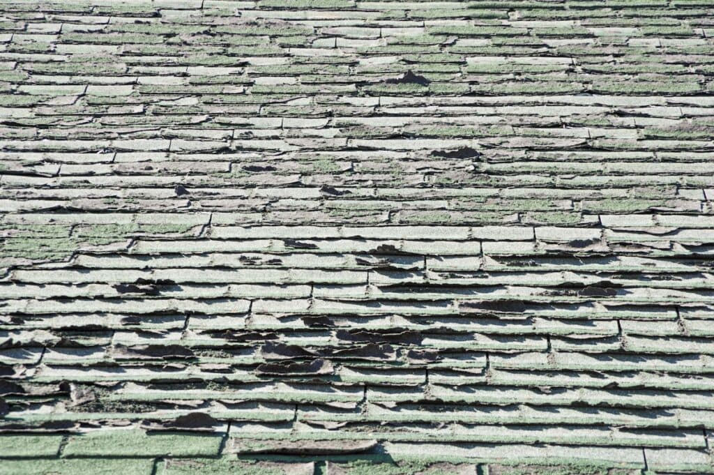 sun damaged old roof with peeling and curling composition shingles