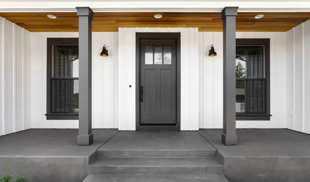 ront door to modern farmhouse home. Home exterior with white vertical wood siding and black front door. Columns and sconce lights on both sides of door.