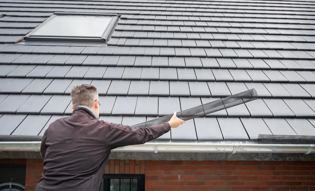 Man puts a gutter mesh to the rain gutter to protect the gutter from leaves.