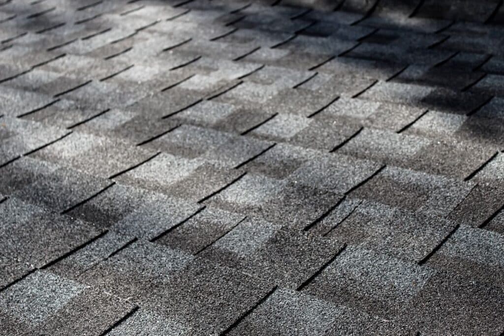 close-up of an asphalt shingle roof at an angle with dappled sunlight