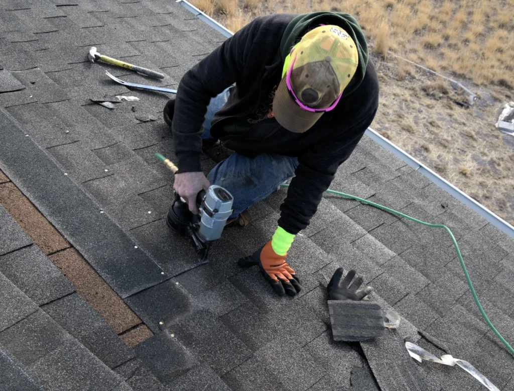 worker using nail gun to place asphalt shingles on roof