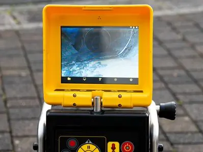A professional plumber monitoring a high-definition video screen displaying the inside of a clean underground pipe