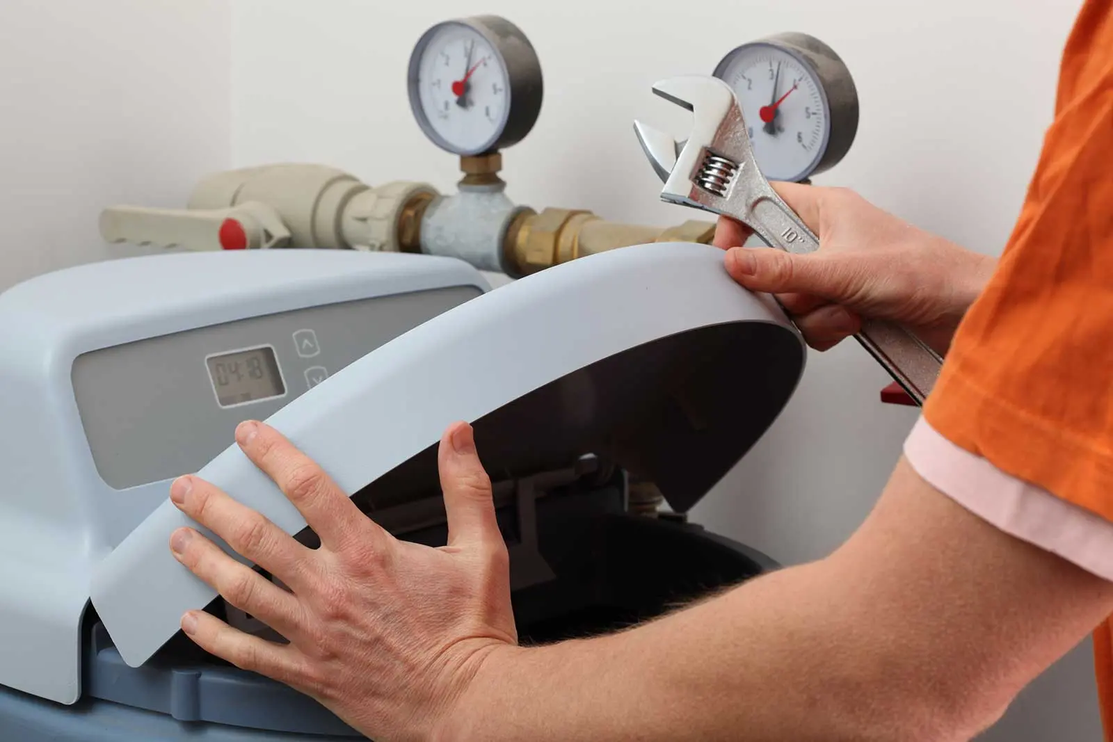 Person using an adjustable wrench on a machine with pressure gauges in an industrial setting for plumbing repair services.