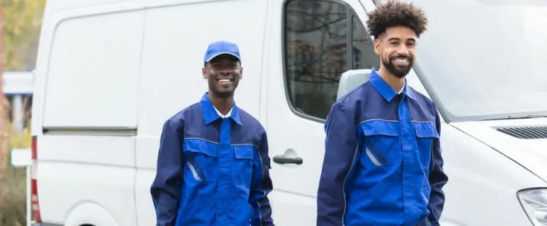 Two smiling plumbers in blue uniforms standing outside a service van, representing Allore's Plumbing Services LLC and their commitment to reliable plumbing assistance.