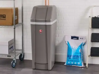Water softener unit beside a bag of salt crystals, illustrating home water treatment solutions for hard water issues.