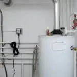 Water heater in a utility space with vent pipe, plumbing, and a wall-mounted phone, showcasing an organized environment.