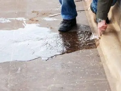 Person inspecting a slab leak with water pooling on concrete floor, highlighting plumbing issues related to home foundations.