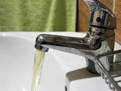 Faucet with yellowish water flowing into a sink, indicating potential water quality issues and the need for a whole-house water filtration system.
