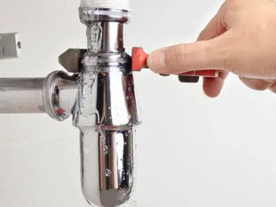 Hand adjusting a valve on a plumbing fixture, with water flowing, illustrating leak repair and plumbing maintenance.