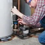 Man repairing a metal water heater with a wrench and cloth; tools essential for home maintenance.