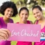 Three women in pink athletic clothing promoting health awareness, holding a card that says "Get Checked.