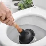 Person using a plunger in a clean bathroom toilet, showcasing effective plumbing tools for home maintenance.
