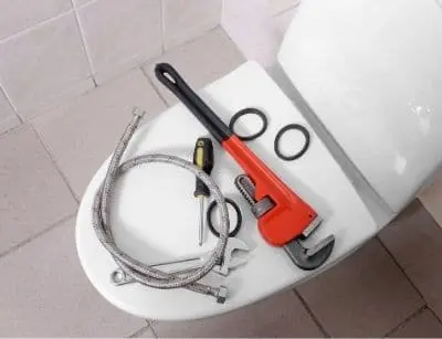 Tools for toilet repair including a wrench, flexible hose, and rubber seals on a toilet seat, emphasizing plumbing maintenance and repair solutions.