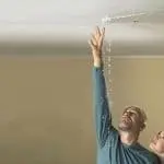 Man examining water leak from ceiling in home, representing plumbing issues addressed by Allore's Plumbing Services LLC.