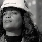 Woman in a hard hat outdoors, showcasing strength and professionalism for a construction business.