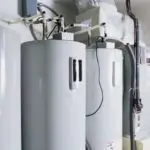 Cylindrical water heaters with control dials in a minimalistic plumbing setup by Allore's Plumbing Services LLC.