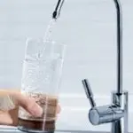 Modern tap faucet pouring water into a clear glass held by a hand, related to Allore's Plumbing Services LLC.