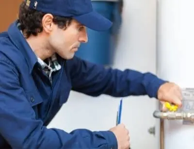 Plumber inspecting a water heater, checking pipe fittings and valves for maintenance issues related to leaks and inefficiencies.